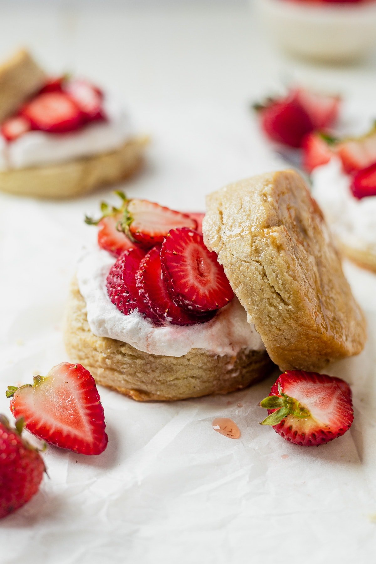 homemade vegan biscuits with fresh strawberries and coconut whipped cream on a piece of parchment paper