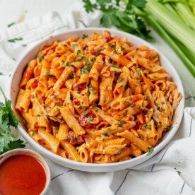 buffalo chicken pasta in a white bowl topped with parsley and surrounded by extra hot sauce and fresh celery