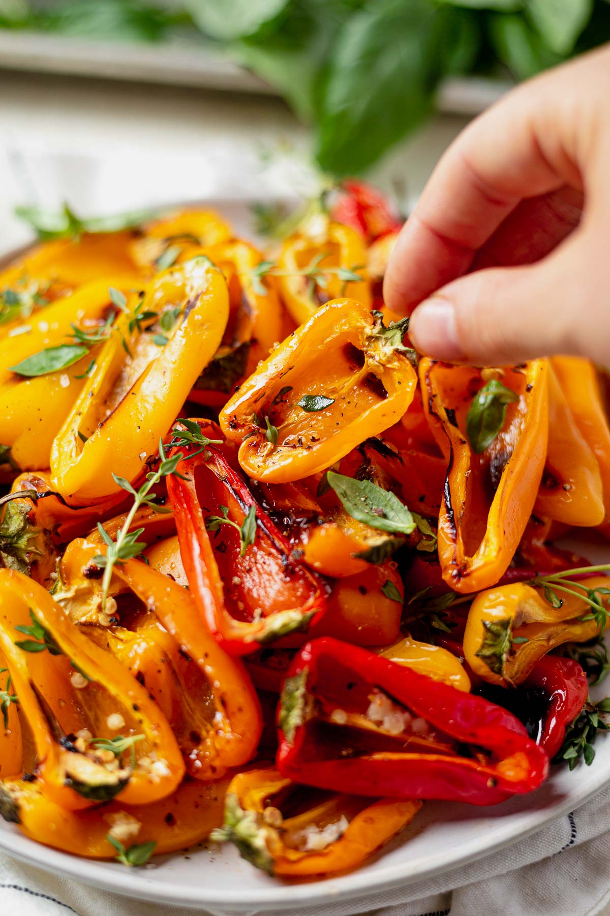 a plate of roasted mini sweet peppers with a woman's hand picking up a yellow pepper off the top