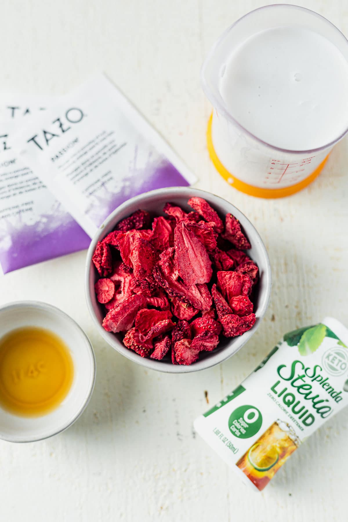 freeze dried strawberries, tazo tea bags, stevia, vanilla and coconut milk on a white table 