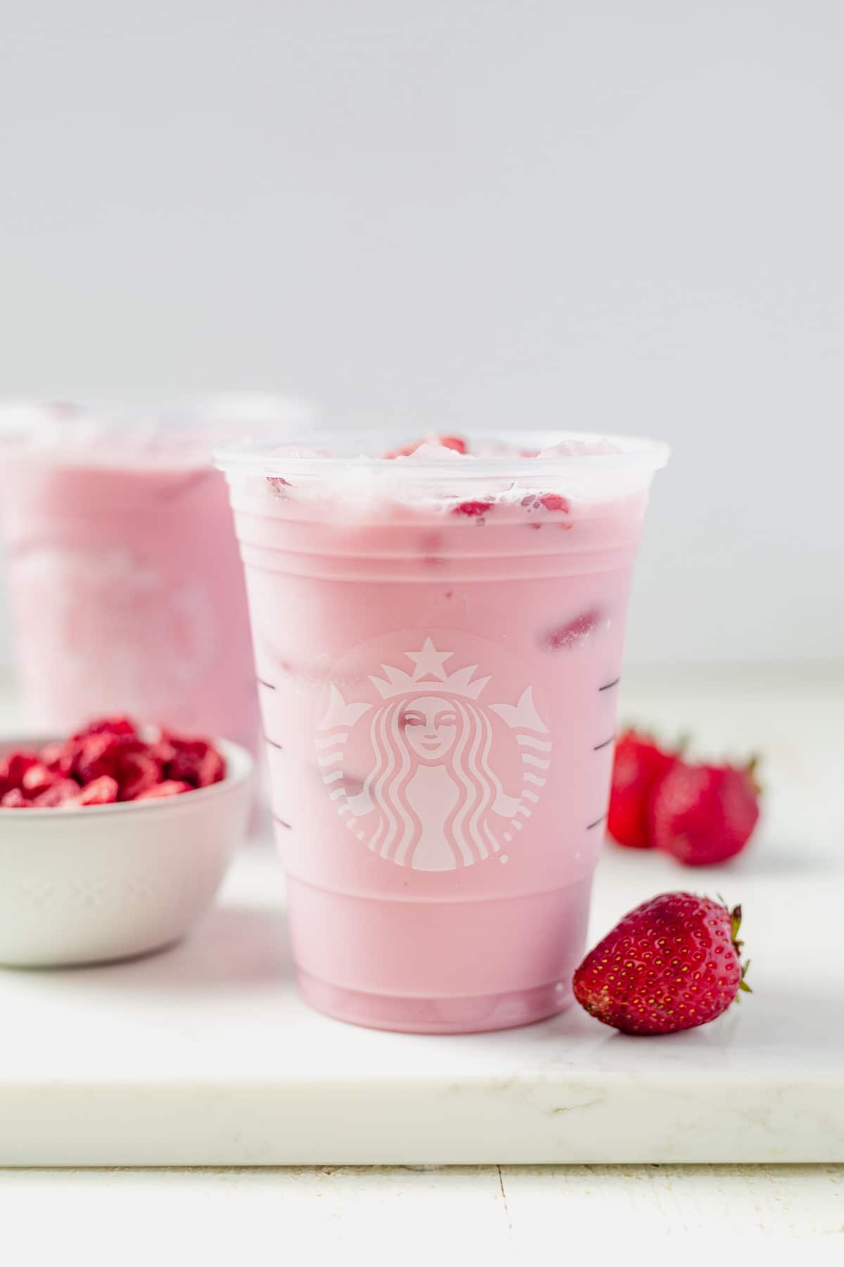 homemade keto pink drink in a starbucks cup with freeze dried strawberries in a bowl 