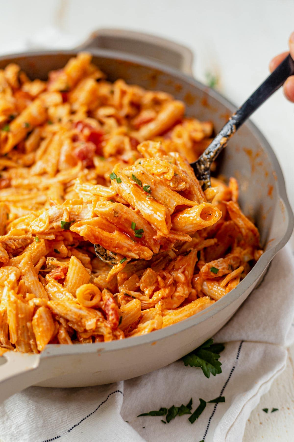 a black spoon scooping out buffalo chicken pasta from a cream colored skillet