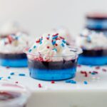 red white and blue jello shots on a white serving tray topped with whipped cream and sprinkles