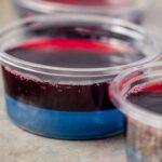 red jello sitting on top a layer of blue jello in a shot cup