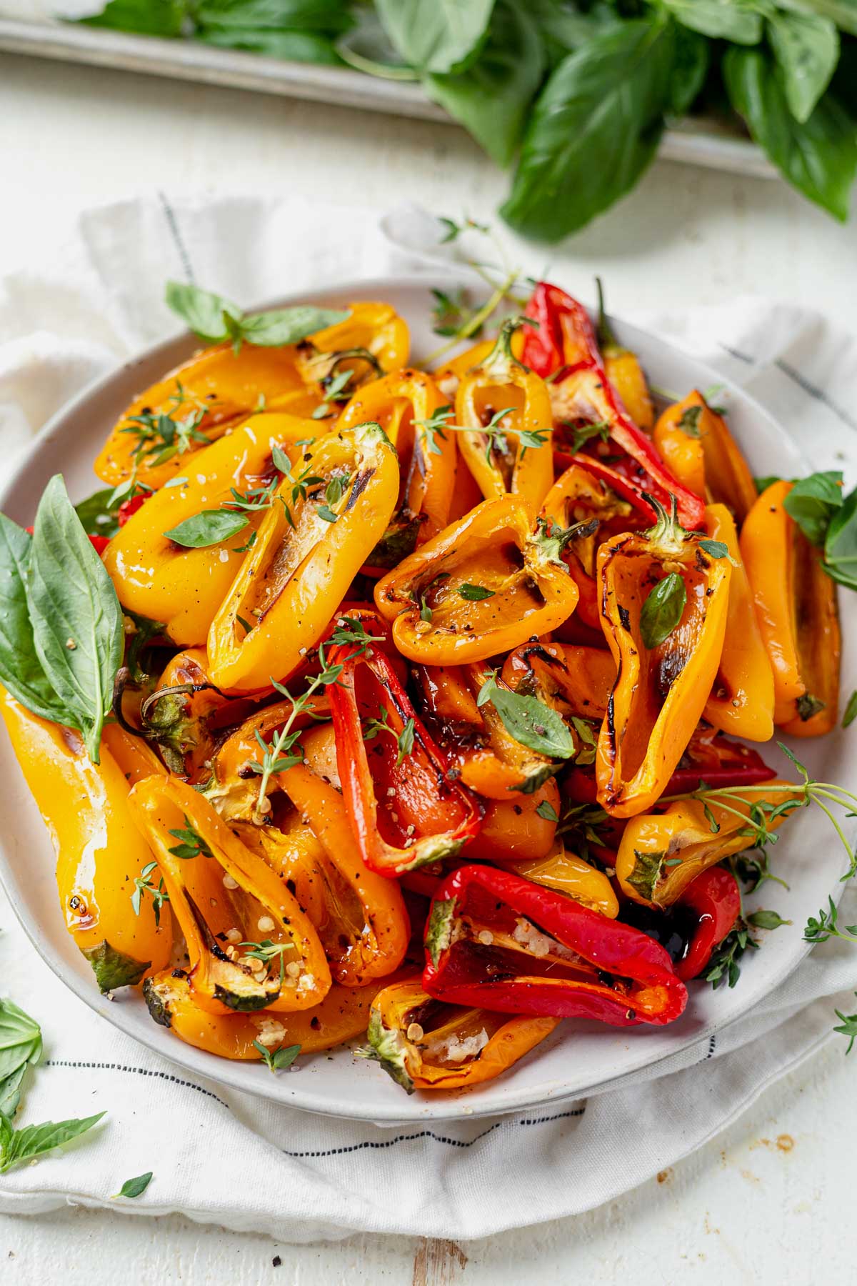 roasted sweet mini peppers cut in half and served on a white dish with fresh basil and thyme