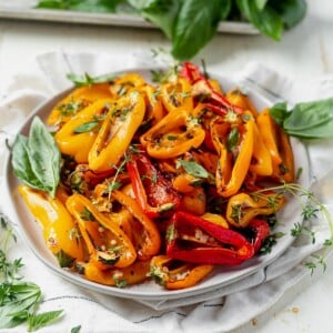 roasted mini sweet peppers on a white plate topped garlic, fresh basil and thyme