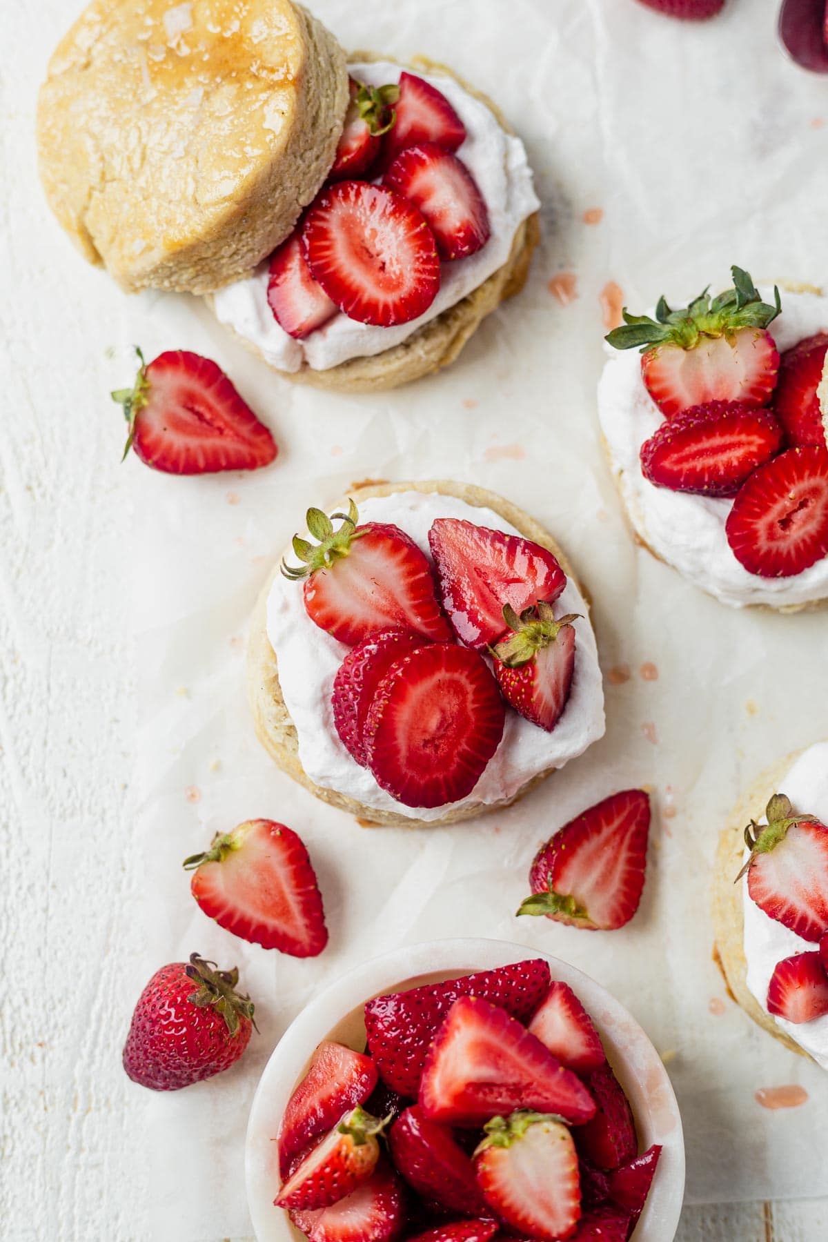 4 vegan strawberry shortcakes on a piece of parchment paper topped with coconut whipped cream
