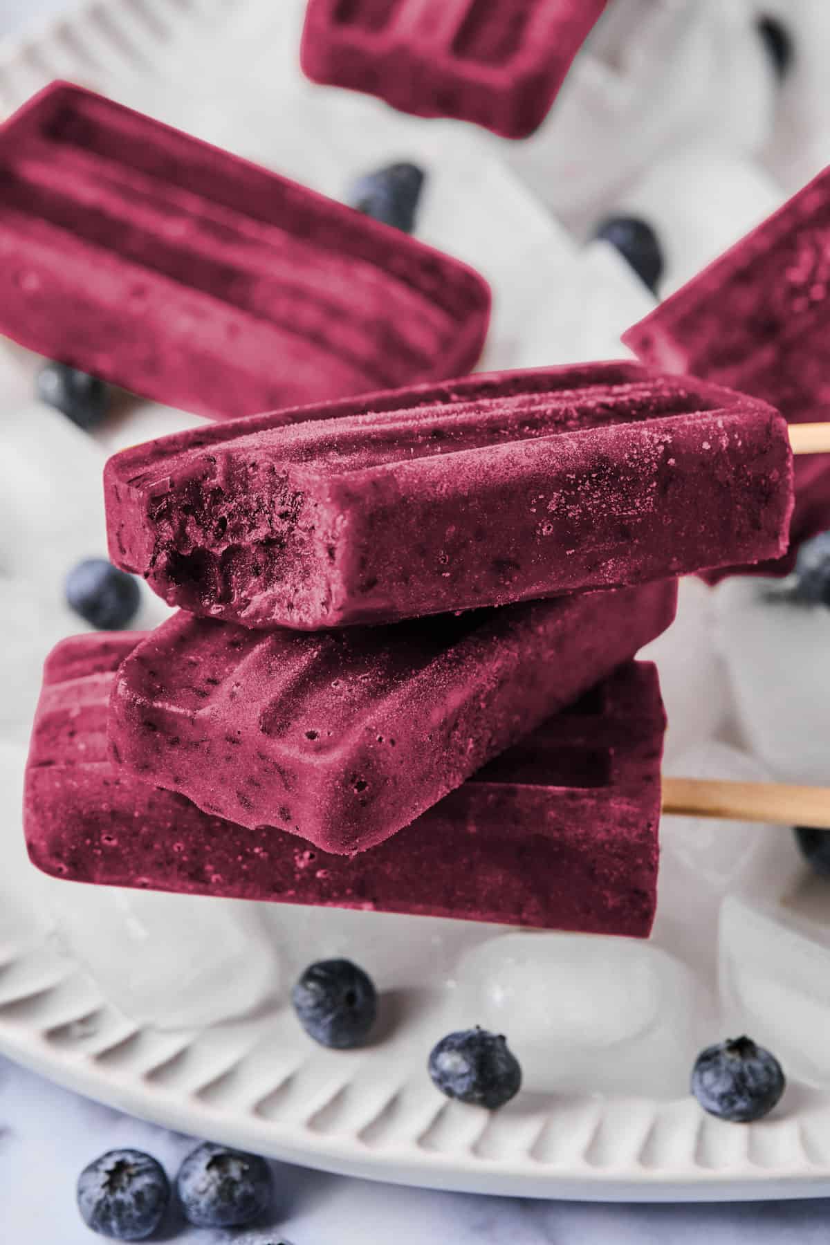 stack of blueberry ice pops on a plate of ice and blueberries