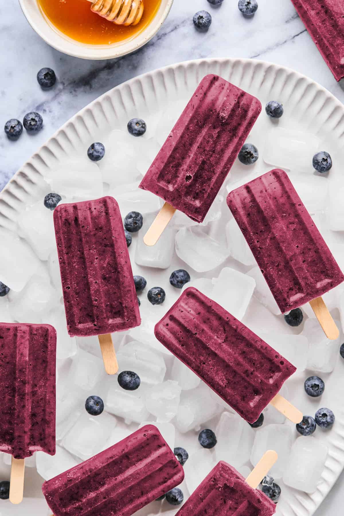blueberry ice pops laying on a layer of ice cubes and fresh blueberries