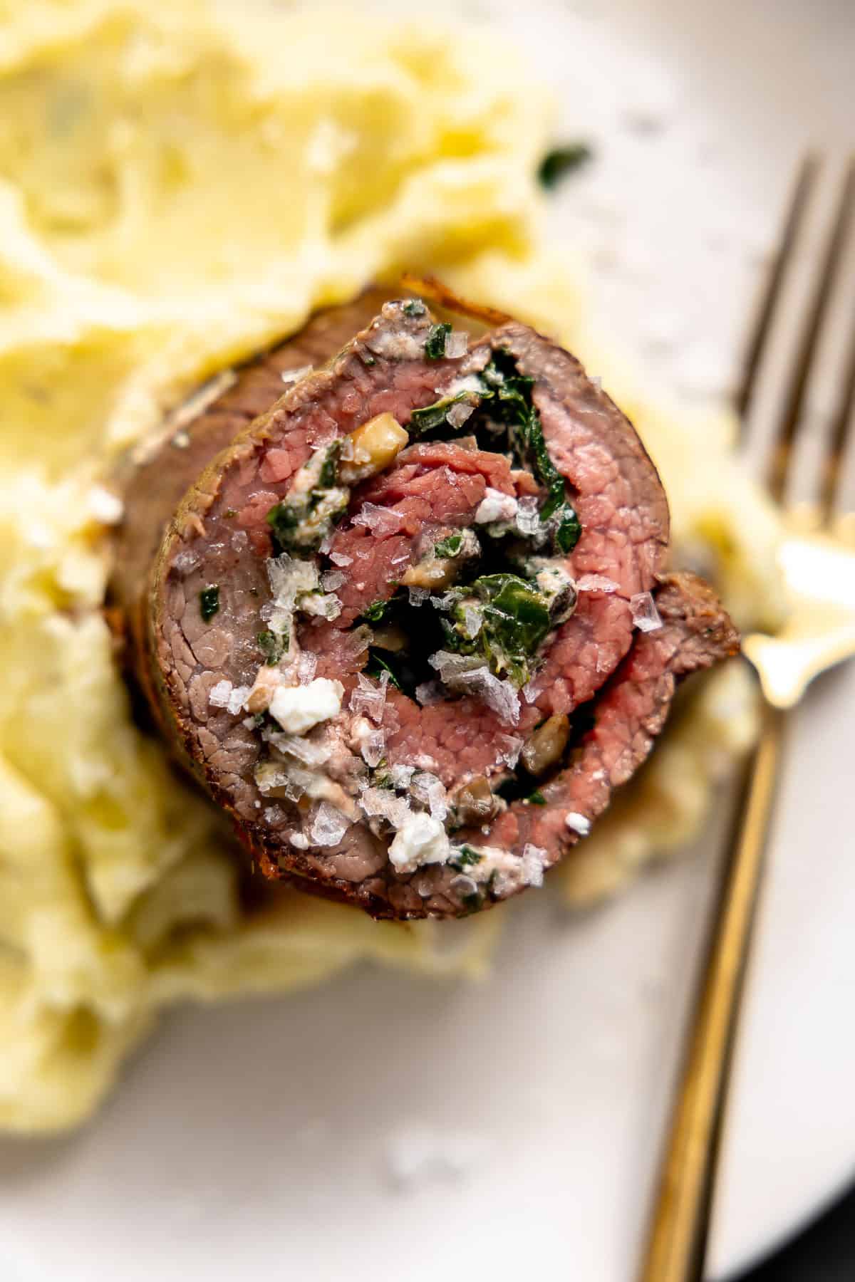 a piece of stuffed flank steak on a plate of mashed potatoes.