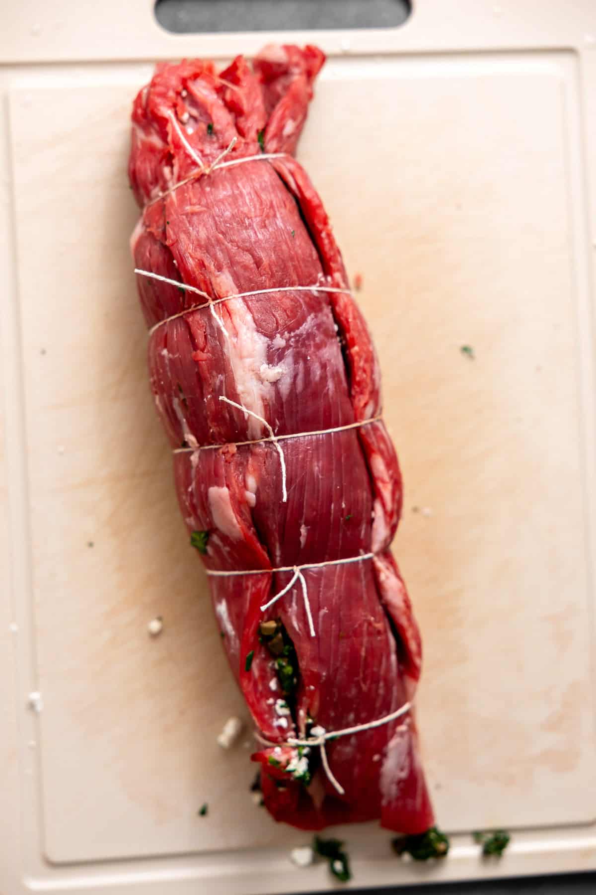 stuffed flank steak rolled and tied on a cutting board.