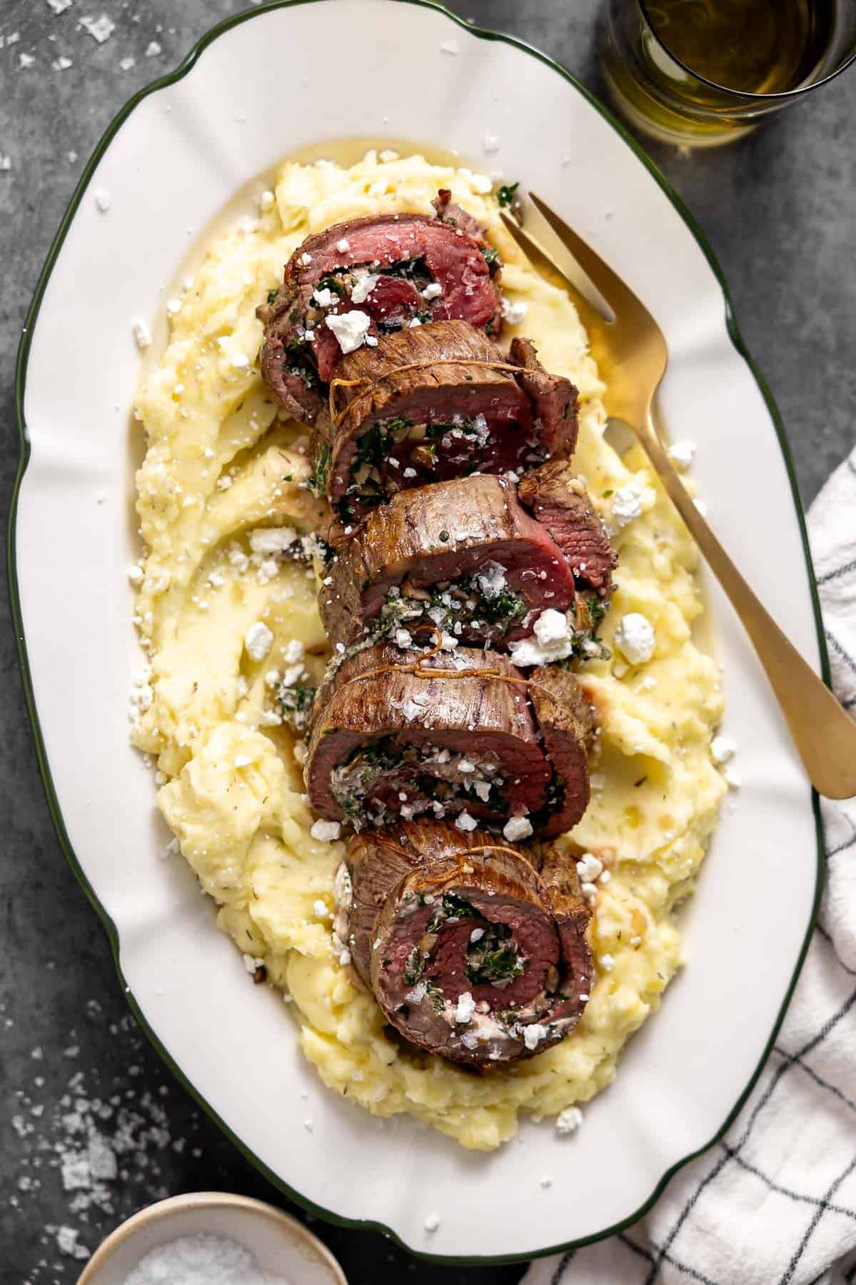 stuffed flank steak cut into rounds on top of a platter of mashed potatoes.