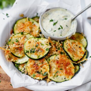 air fryer zucchini chips on a white plate topped with parsley and ranch on the side