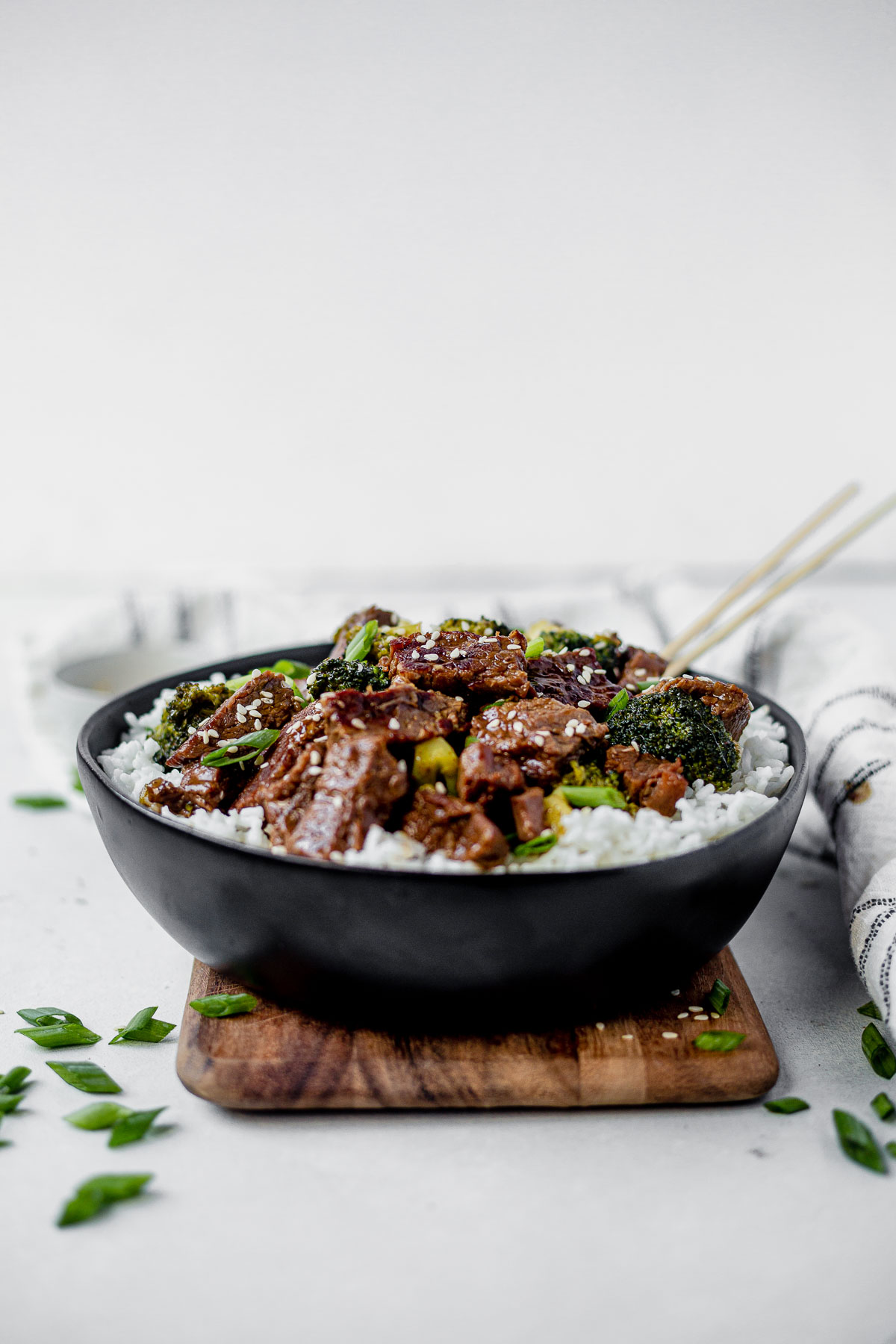 a black bowl full of mongolian beef and broccoli with chop sticks