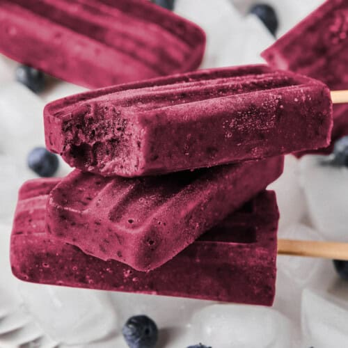 three homemade blueberry popsicles stacked on a bowl of ice.