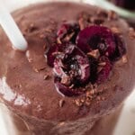 cherry avocado smoothie in a glass with a white straw.