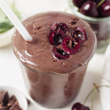 chocolate cherry smoothie in a glass topped with fresh cherries and shaved chocolate