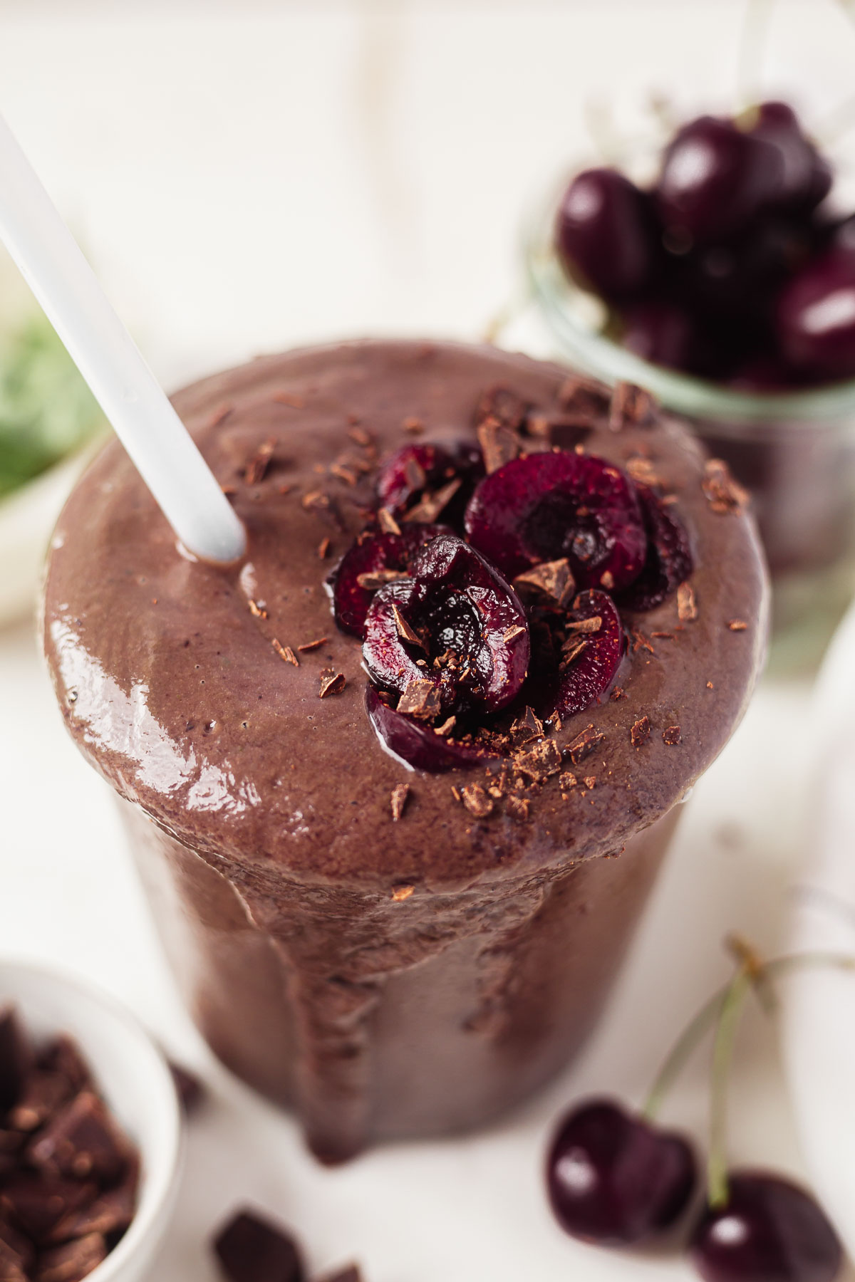 chocolate cherry smoothie overflowing out of a glass cup with a straw