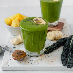kale smoothie overflowing from a glass with fresh banana and chia seeds