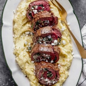 a platter of mashed potatoes and stuffed flank steak with a serving fork.