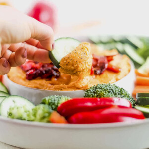 dipping a cucumber into sweet potato hummus