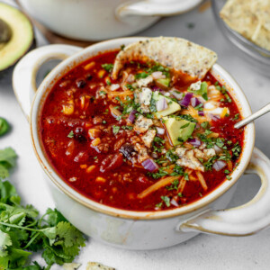 a bowl of instant pot taco soup with avocado, cilantro, tortillas and cheese on top