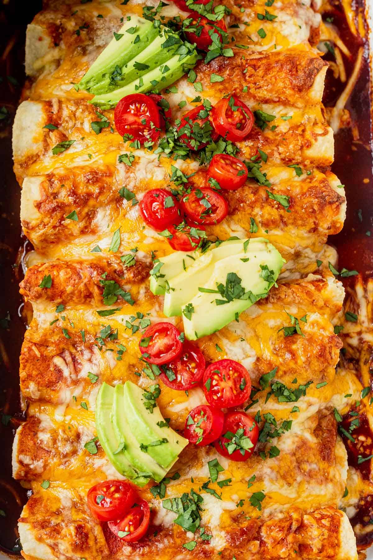 healthy chicken enchiladas in a casserole dish with avocado and tomato