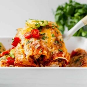 spatula pulling two healthy chicken enchiladas out of the pan