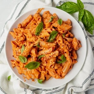 creamy penne arrabbiata in a white bowl topped with basil