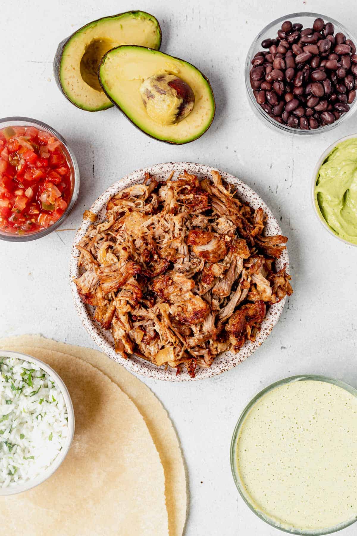 a bowl of instant pot carnitas on a countertop with toppings 