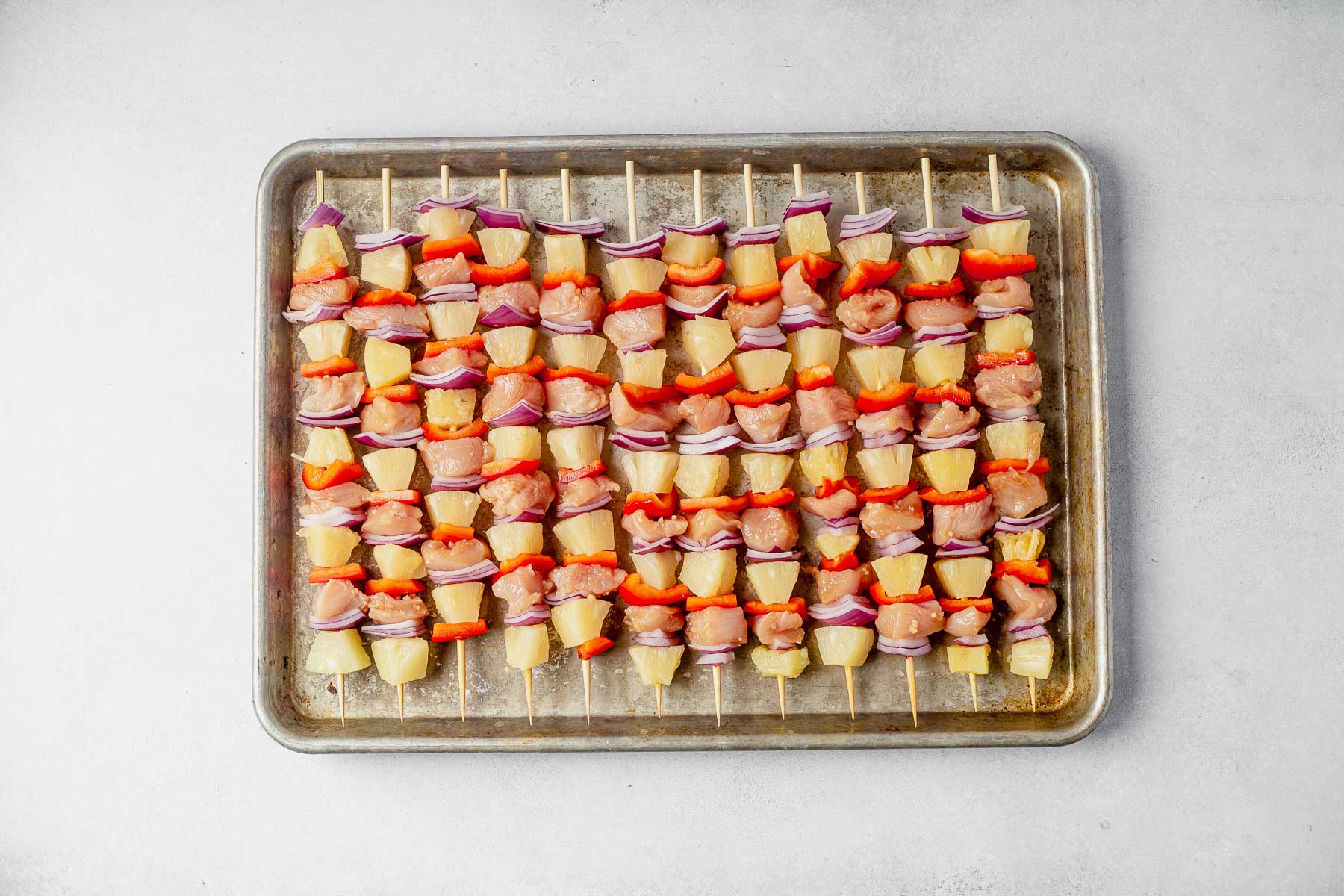 uncooked hawaiian chicken kabobs lined up on a sheet pan before cooking