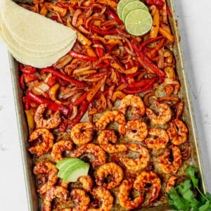 sheet pan shrimp fajitas on a white table with tortillas and avocado