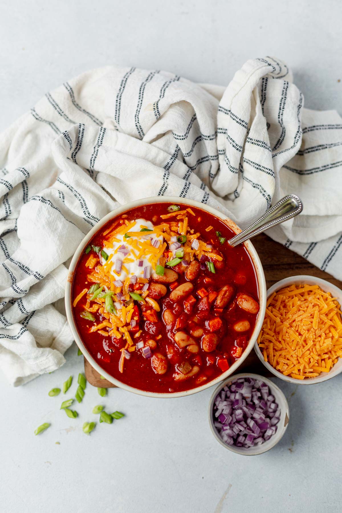 slow cooker vegetarian chili in a white bowl with shredded cheese and onion next to it