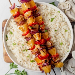 three hawaiian chicken kabobs on top of a bowl of coconut rice