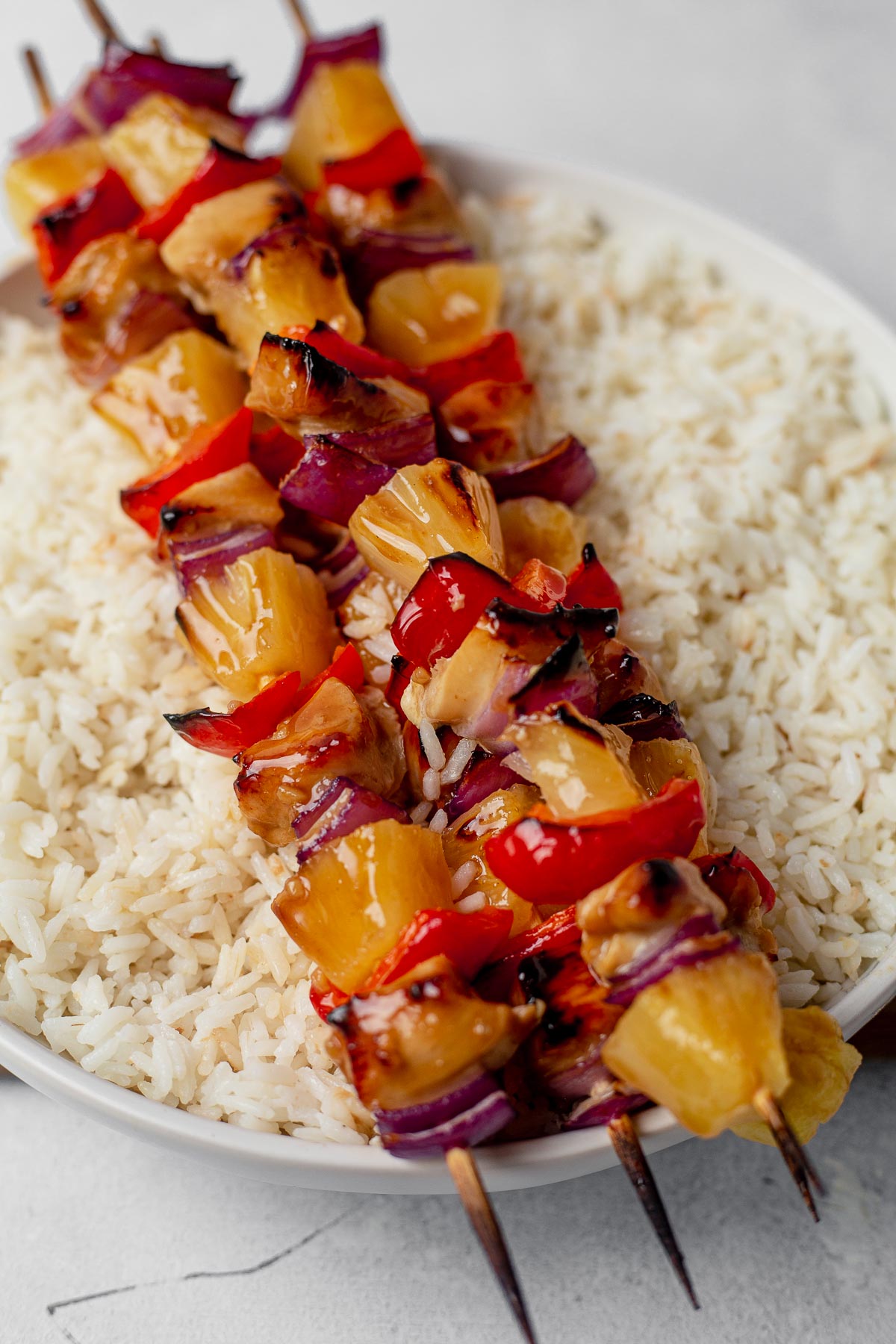 three hawaiian chicken kabobs sitting on top of a bowl of coconut rice