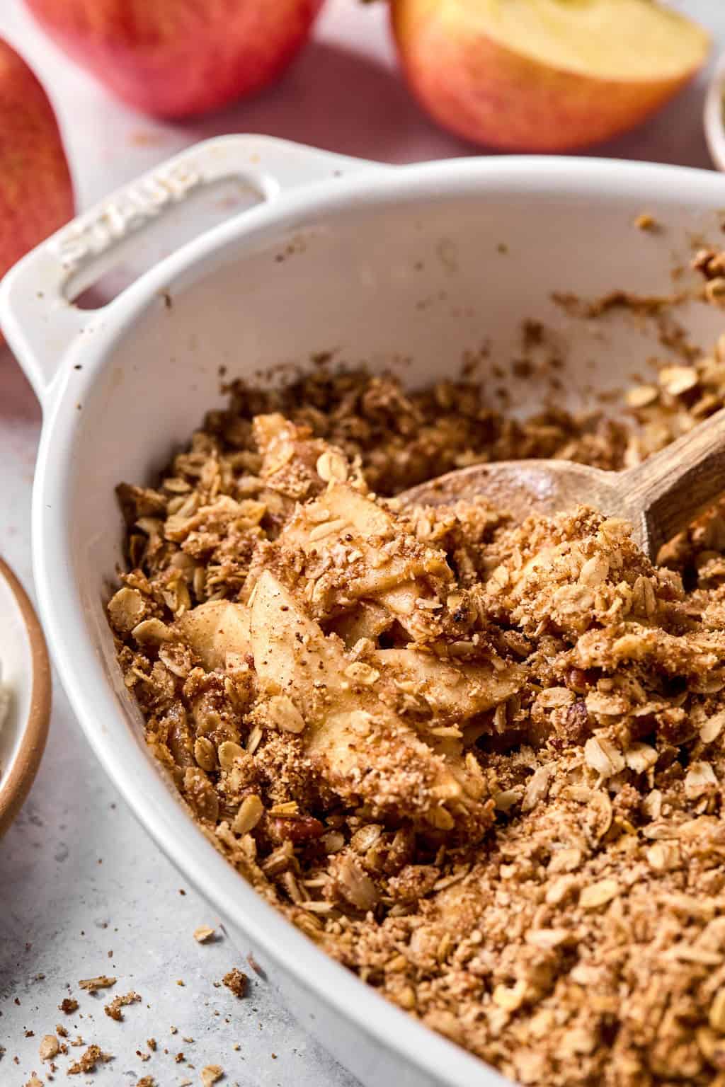 wooden spoon scooping out healthy apple crisp from a baking dish.