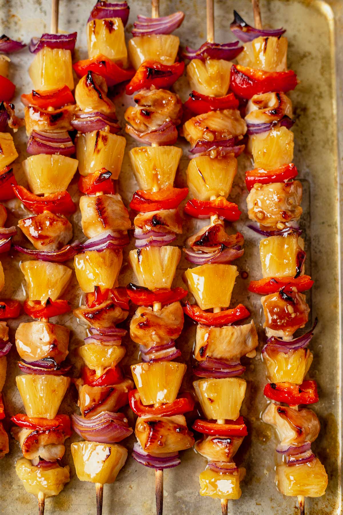 5 crispy charred hawaiian chicken kabobs on a sheet pan layered with peppers