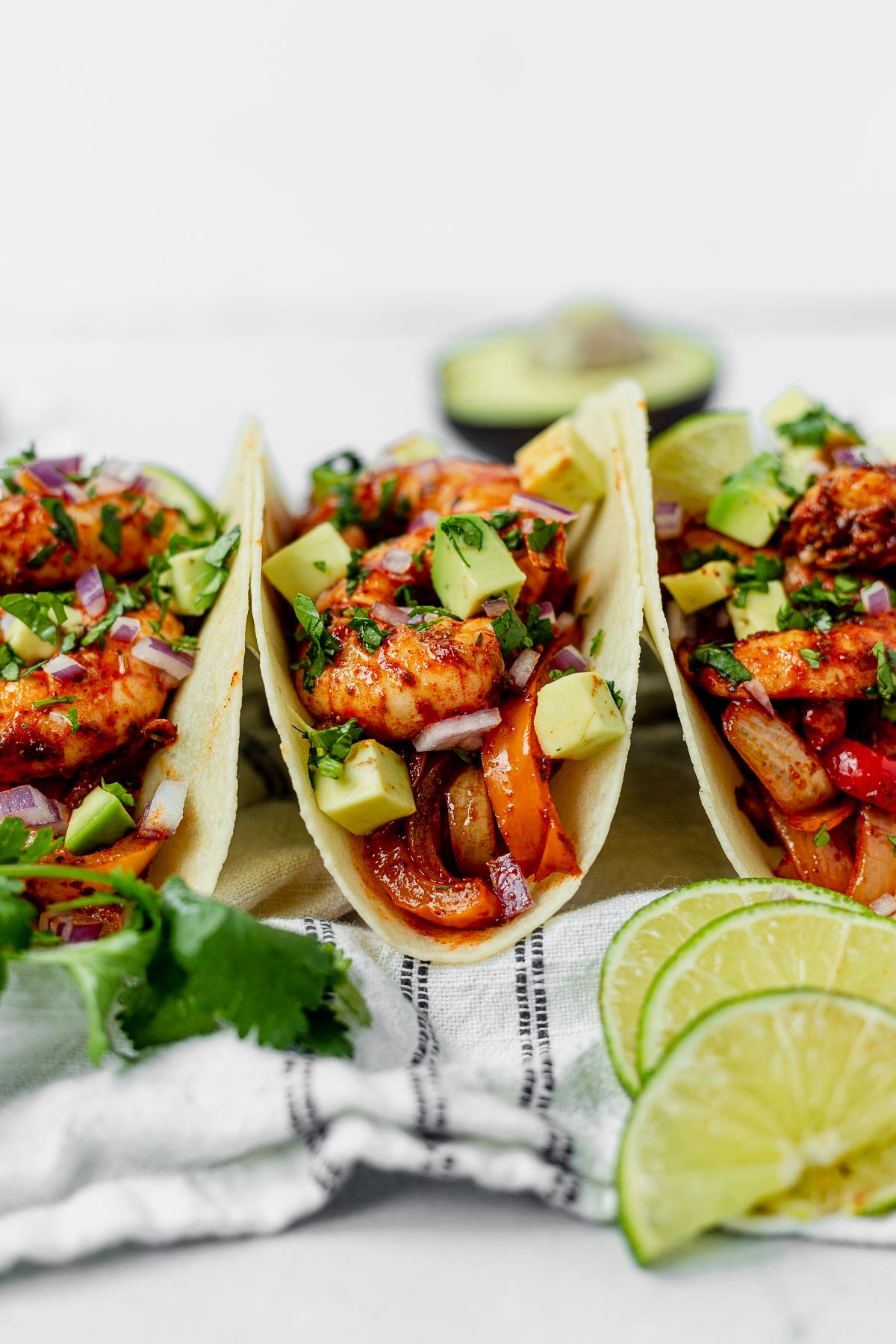 three sheet pan shrimp fajitas topped with avocado and cilantro