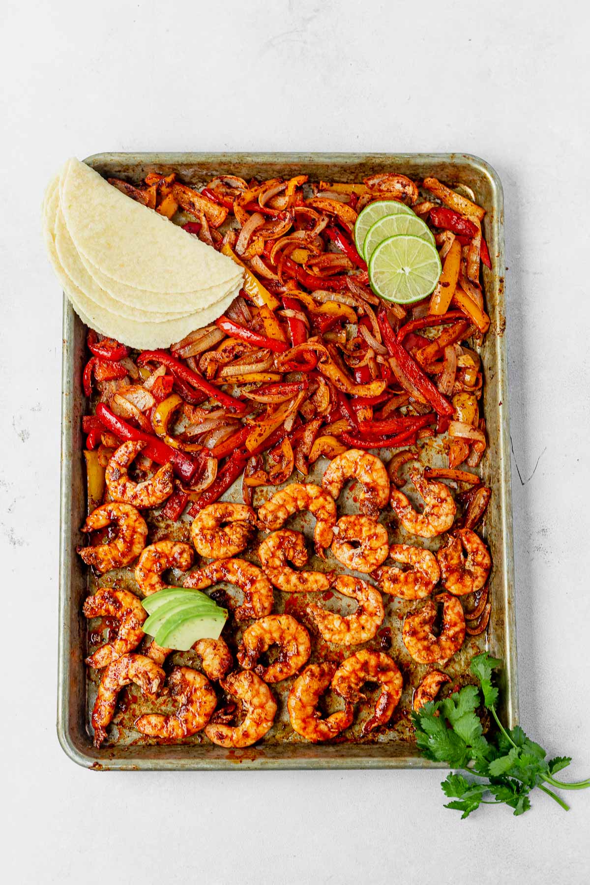 sheet pan shrimp fajitas with taco shells, avocado and cilantro on the side