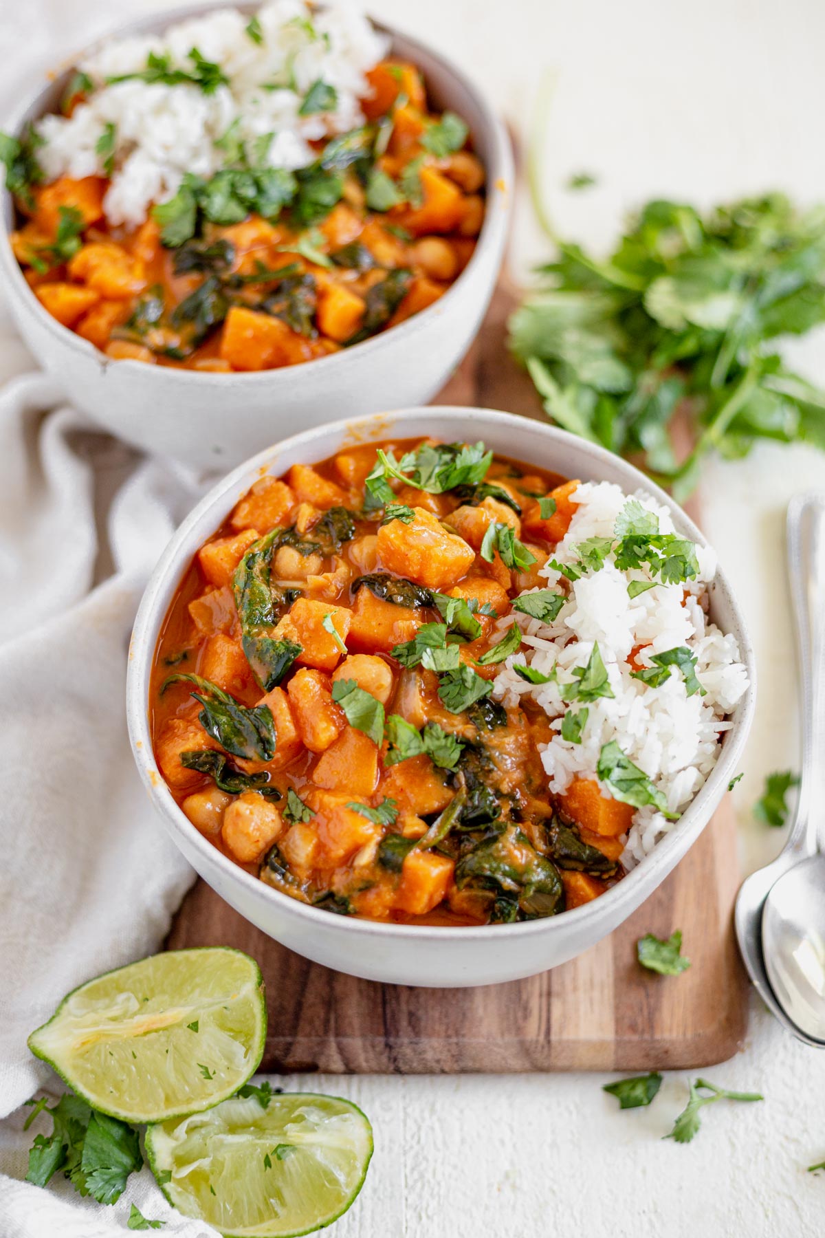 two white bowls full of sweet potato chickpea curry topped with cilantro and fresh limes