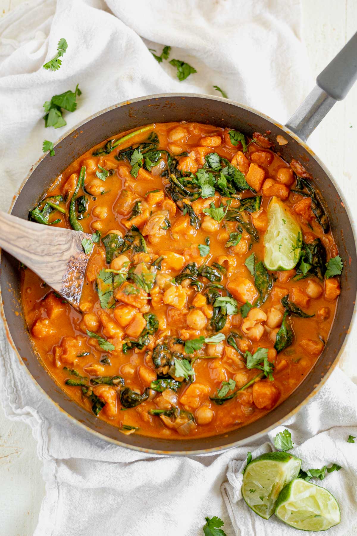 a wooden spoon scooping out a serving of sweet potato and chickpea curry from a pan