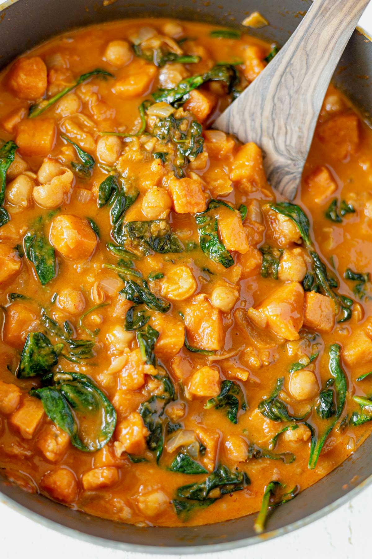 sweet potato curry with chickpeas and spinach in a large pan with a wooden spoon