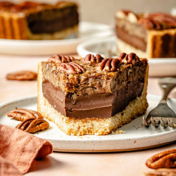 a slice of chocolate paleo pecan pie on a plate with a bite missing showing the crust, chocolate ganache, and pecan pie layers.