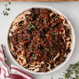 beef short rib pasta tossed in a white bowl served with fresh thyme