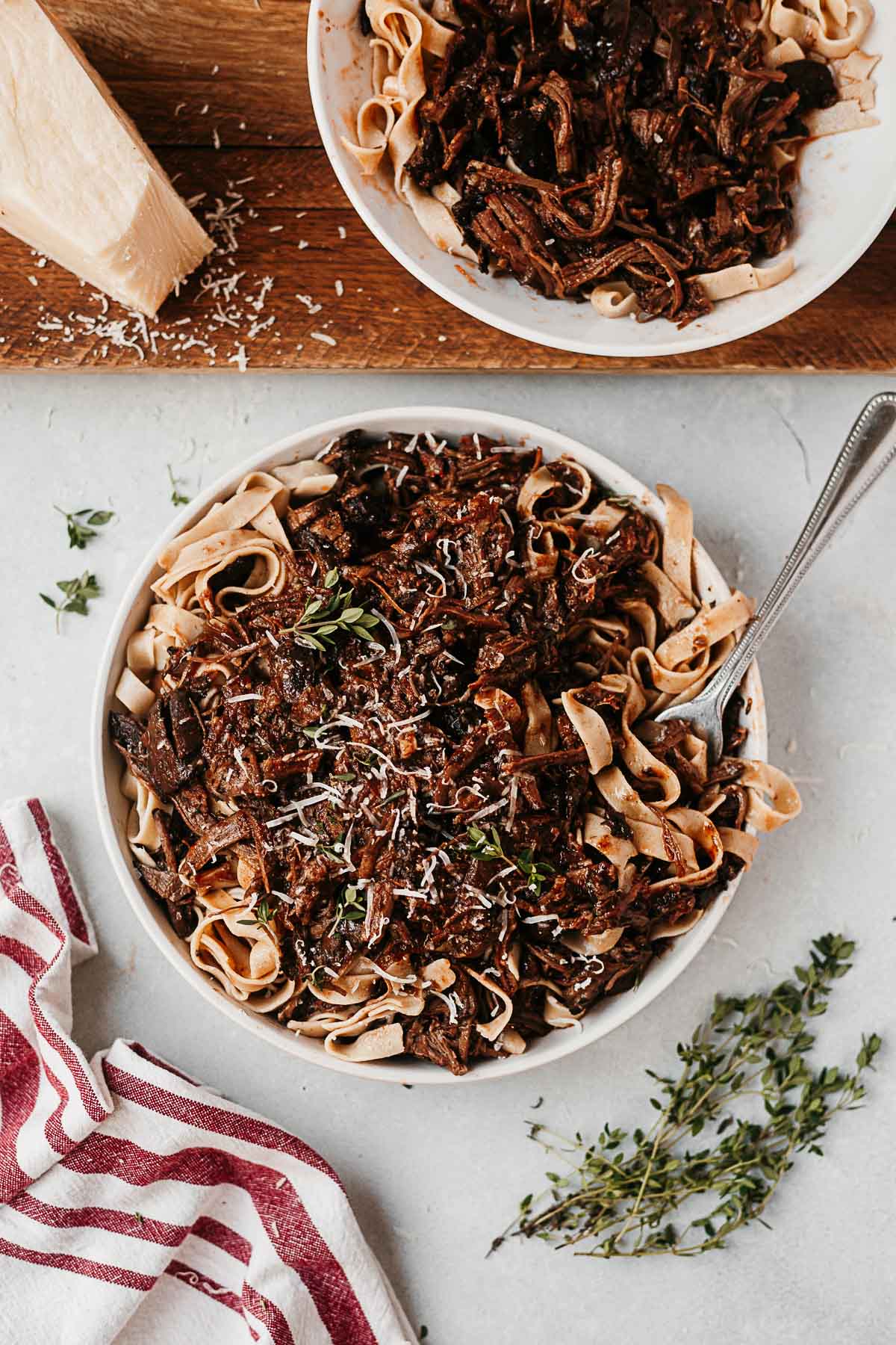 short rib pasta in a white bowl topped with fresh thyme and parmesan