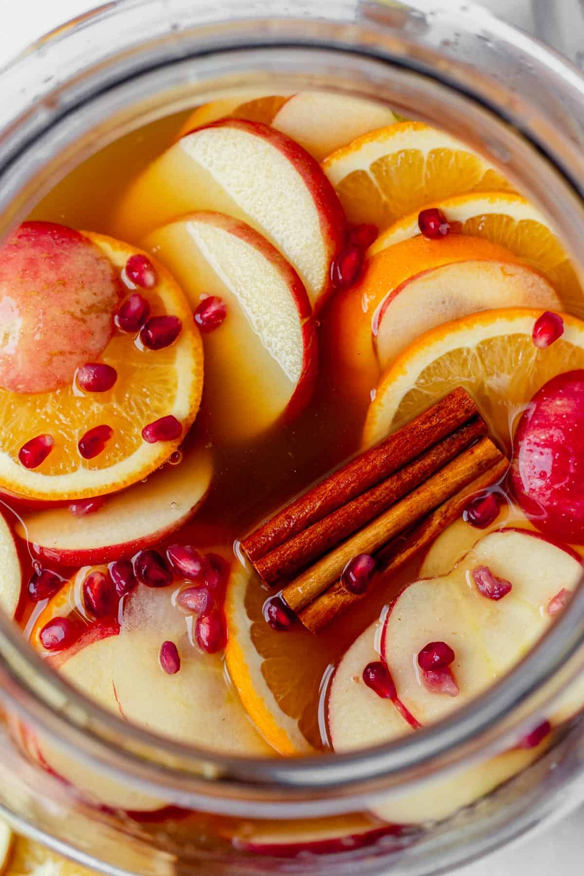 apple cider sangria recipe in a large glass pitcher with cinnamon sticks.