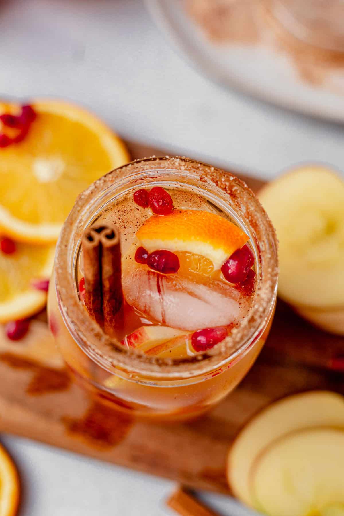 a glass of apple cider sangria in a mason jar with pomegranates and apple slices.