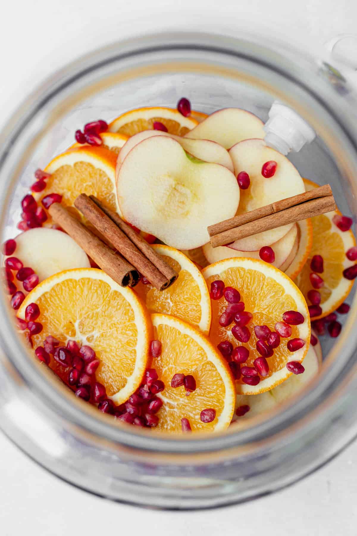 oranges, apples, pomegranates, and cinnamon sticks in a pitcher.