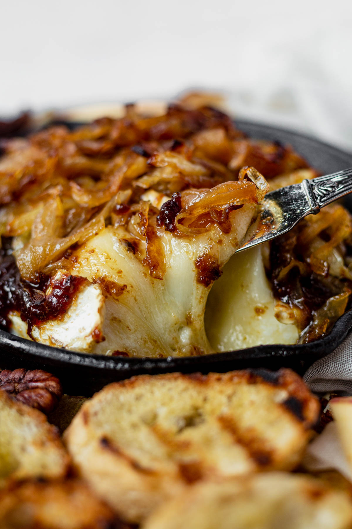 a cheese knife scooping out a portion of baked brie with fig jam from a cast iron skillet