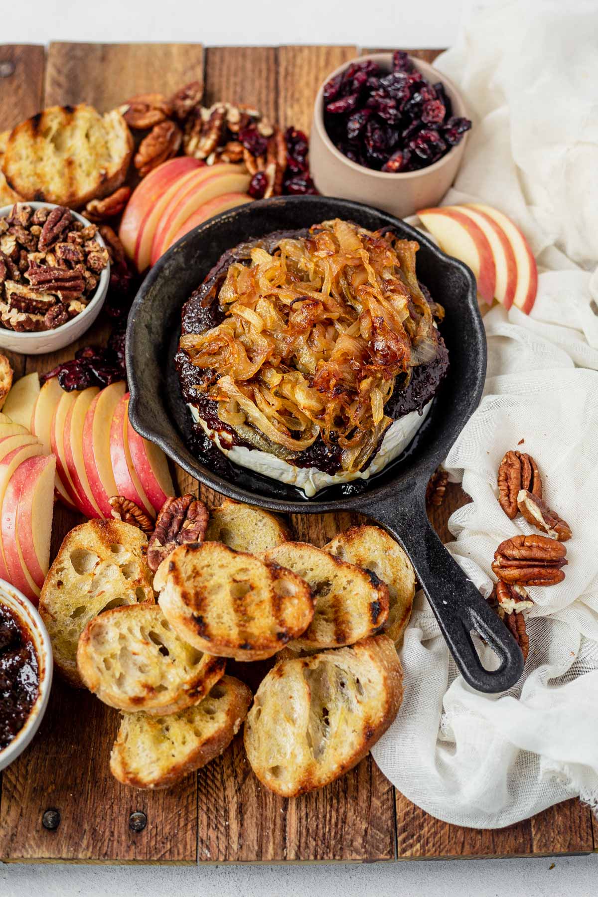 baked brie with fig jam and caramelized onion on a cheese board with apples, nuts and a sliced baguette